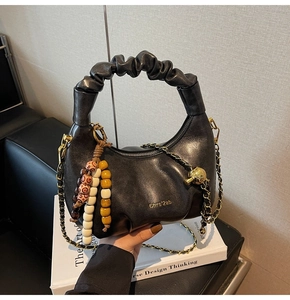 Detail of black leather dumpling bag with ruched handle and golden chain strap