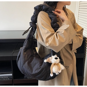 Detailed view of black quilted dumpling bag with scrunchie strap and plush charm