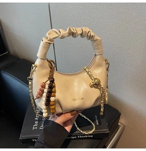 Detail of cream pleated crescent bag with gold chain strap and wooden bead charm accessory