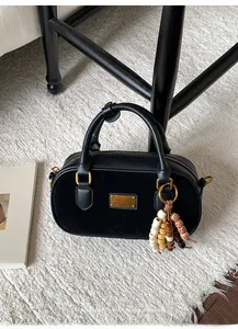 Détail d'un sac boston en cuir et daim noir avec plaque dorée et breloque en perles