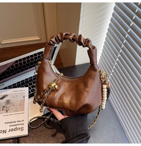 Detailed view of brown ruched handle bag with gold chain strap and pearl bead charm