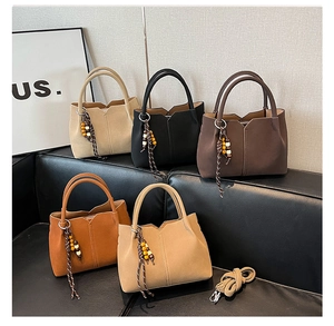 Detail of five suede bucket bags in various colors with metallic bead charms on a sofa