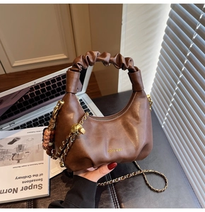 Detail of dark brown hobo bag with pleated handle, gold chain, and wooden bead charm accessory