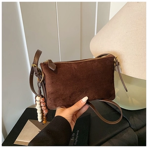 Detalle de bolso bandolera de cuero esmerilado marrón oscuro con borla y cremallera metálica