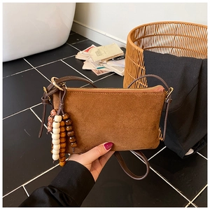 Detalle de bolso bandolera pequeño en ante marrón mate con borla de cuentas de madera color