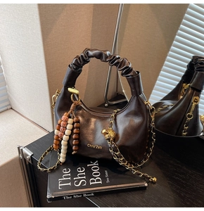 Detail of dark brown dumpling bag with pleated handle, gold chain, and beaded tassel