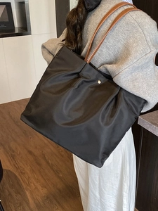 Chic black nylon tote bag with brown leather straps shown on a model in a minimalist room