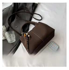 Detail view of dark brown matte bucket bag with a wooden bead charm and long shoulder strap