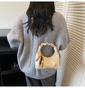Detail of off-white dumpling bag with pleated handle and beaded charm on knitted sweater