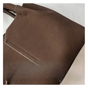 Close-up of brown litchi textured leather handbag showing precise stitching details