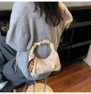 Detail of cream pleated dumpling bag with scrunchie handle and gold chain strap