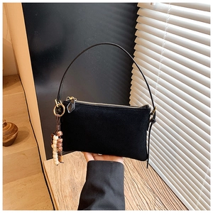 Detalle de bolso de hombro en ante negro con cremallera dorada y colgante de cuentas