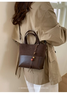 Detail of a dark brown suede and leather crossbody bucket bag worn by a model