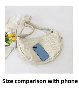 Detail view of cream pleated crescent bag showing capacity comparison with a smartphone