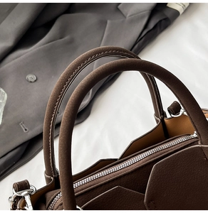Detailed close-up of dark brown suede bucket bag with silver zipper and geometric panels