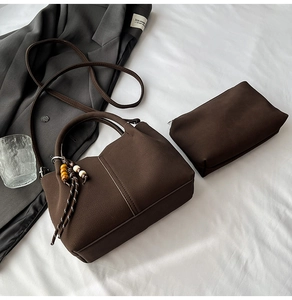 Detail of dark brown faux suede handbag set with cylindrical handle and wooden bead charm