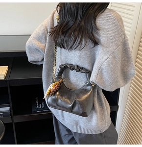 Detail of dark grey pleated leather bag with gold chain and beaded charm on model