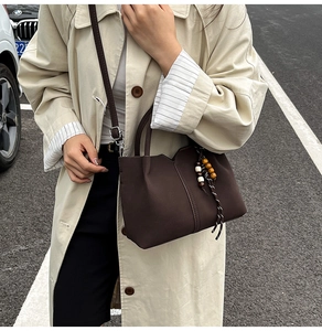 Detail of dark brown leather bucket bag with pleated texture and colorful beaded tassel