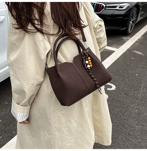 Detail of dark brown geometric shoulder bag with colorful bead charm on beige coat