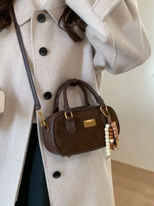 Sac cylindrique marron avec poignées et breloque en perles porté par mannequin