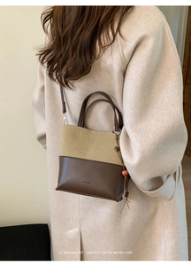 Detail of two-tone bucket bag with suede texture and pearl charm on a model's shoulder