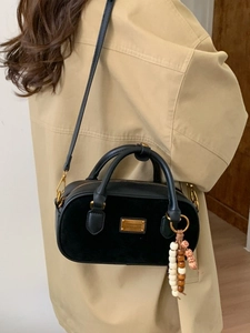 Sac Boston noir avec plaque dorée et breloque perlée porté par un mannequin