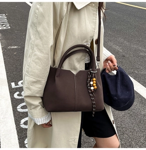Outdoor shot of dark brown minimalist leather handbag with a woven beaded tassel pendant