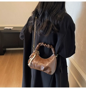 Detail of dark brown leather handbag featuring pleated cloud handle and beaded pendant