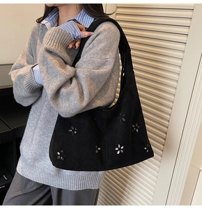 Détail du sac cabas en daim noir avec motif de fleurs ajourées et rivets sur le côté