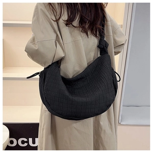 Detail of black pleated tote bag with knotted shoulder strap on model in trench coat