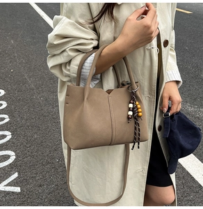Detail view of khaki leather bucket bag with wooden bead charm and crossbody strap