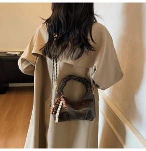 Detail of dark brown pleated dumpling bag with golden chain and beaded pendant