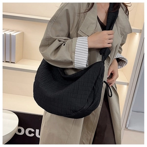 Detail of black quilted shoulder bag featuring square texture and wide knotted strap