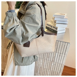 Close-up of beige suede tote with brown leather trim and adjustable metal buckle