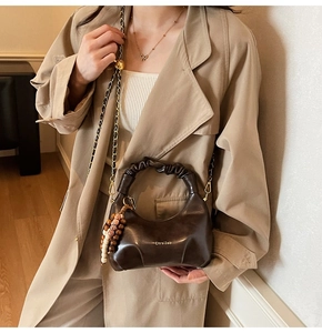 Detail of dark brown leather handbag featuring pleated handles and gold chain strap
