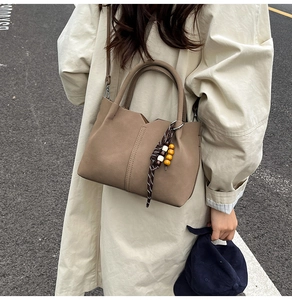 Detail of a beige leather bucket bag with braided strap and wooden bead accessory