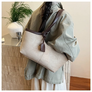 Detail view of large canvas tote bag with brown leather trim worn by model in a room
