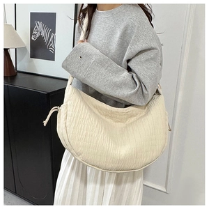 Detail shot of a cream hobo bag with pleated texture and drawstring accents worn by model