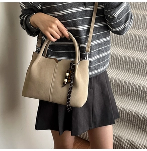 Macro shot of beige leather bucket bag with vertical stitching and beaded tassel charm