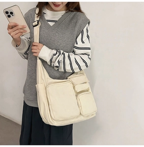 Vue détaillée du grand sac messager en toile crème avec poches et large bandoulière noire