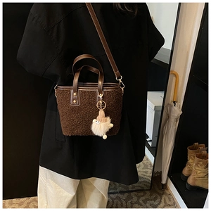 Brown fluffy bucket bag worn crossbody with a cute gnome plush pendant on detail