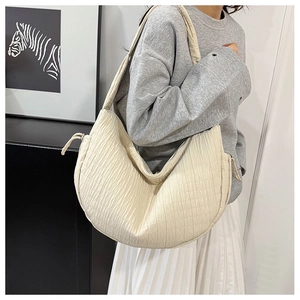 Detail of a creamy white crescent tote bag with unique pleated textures and drawstring