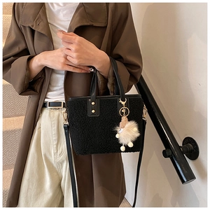 Detail of plush black bucket bag with soft fleece texture and cute cream charm