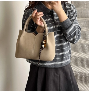 Detail of beige bucket bag featuring wavy rim and decorative wood bead tassel charm