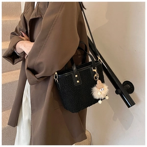 Close-up of black plush bucket bag with monster charm and leather shoulder strap