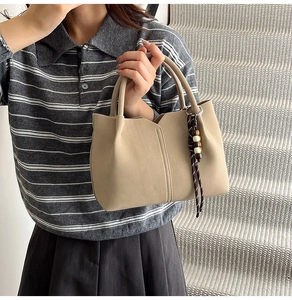 Detail showing the lychee grain texture and boho beaded charm on a beige handbag