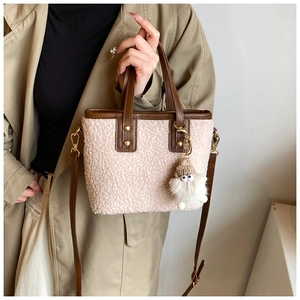 Detail of plush beige bucket bag with brown leather trim and cute white pompom charm