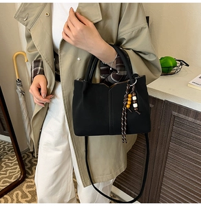 Detail of black crossbody bucket bag with bohemian tassel and beaded charm accessory