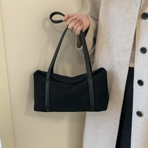 Detail view of a black minimalist suede shoulder bag styled on a beige coat model