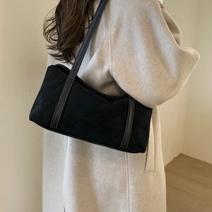 Detail of vintage black suede shoulder bag with leather strap on a beige coat background
